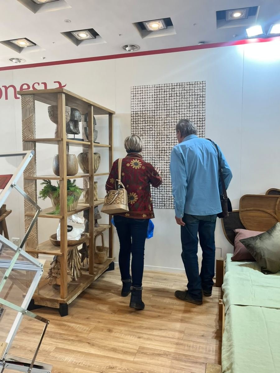 Two visitors viewing a white coconut shell mosaic wall panel at the Indonesia Pavilion