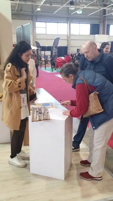 Booth staff assisting visitors registering interest beside teak wall cladding samples on a white pedestal at HOMEDesign Budapest 2025