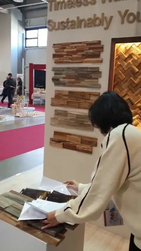 Visitor reviewing documents at a white pedestal in front of mounted teak wall panel samples and Timeless Wall Sustainably You lettering, HOMEDesign Budapest