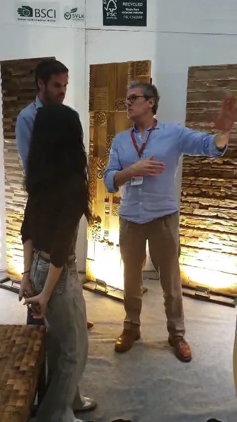 Exhibitor explaining textured teak wall panels and mosaics under BSCI, SVLK and FSC Recycled logos to visitors at the IFEX booth