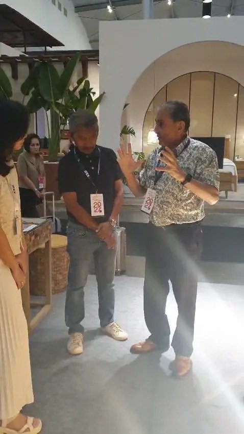 Buyer meeting at the SOSI IFEX booth with teak mosaic furniture in the foreground and tropical plants beside the arched display
