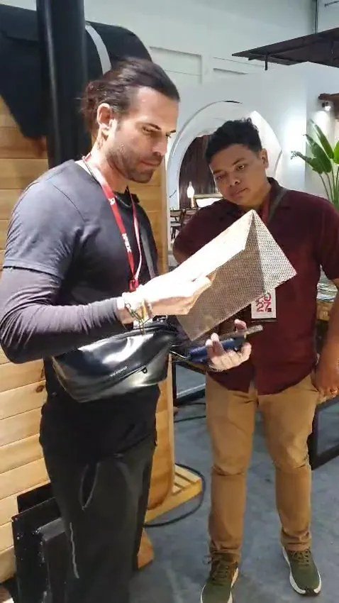 Buyer examining a textured mosaic wall panel sample with barrel pinewood sauna visible in the background at IFEX