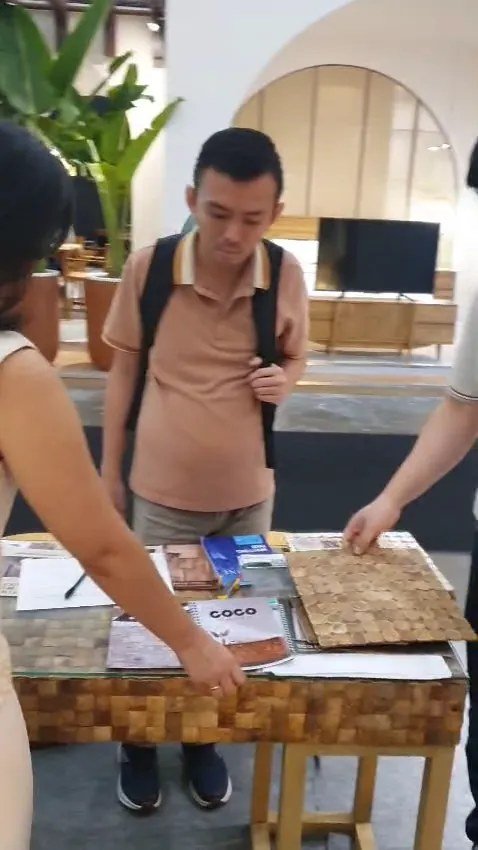 Visitor reviewing COCO coconut shell mosaic brochures and a mosaic sample board on a teak mosaic table at the IFEX booth