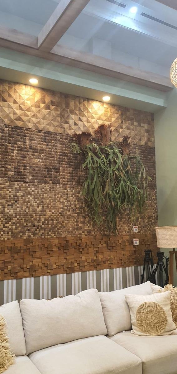 Floor-to-ceiling wall of coconut shell mosaic panels above 3D teak block cladding behind a lounge sofa, KKI 2026