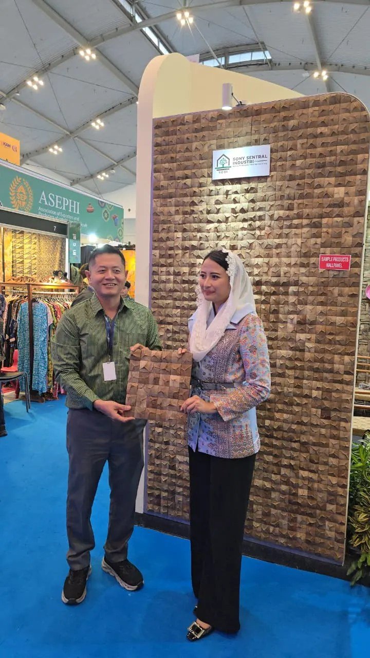 SOSI staff and visitor holding a 3D teak wall panel sample in front of the Sony Sentral Industri display wall, Trade Expo Indonesia 2025
