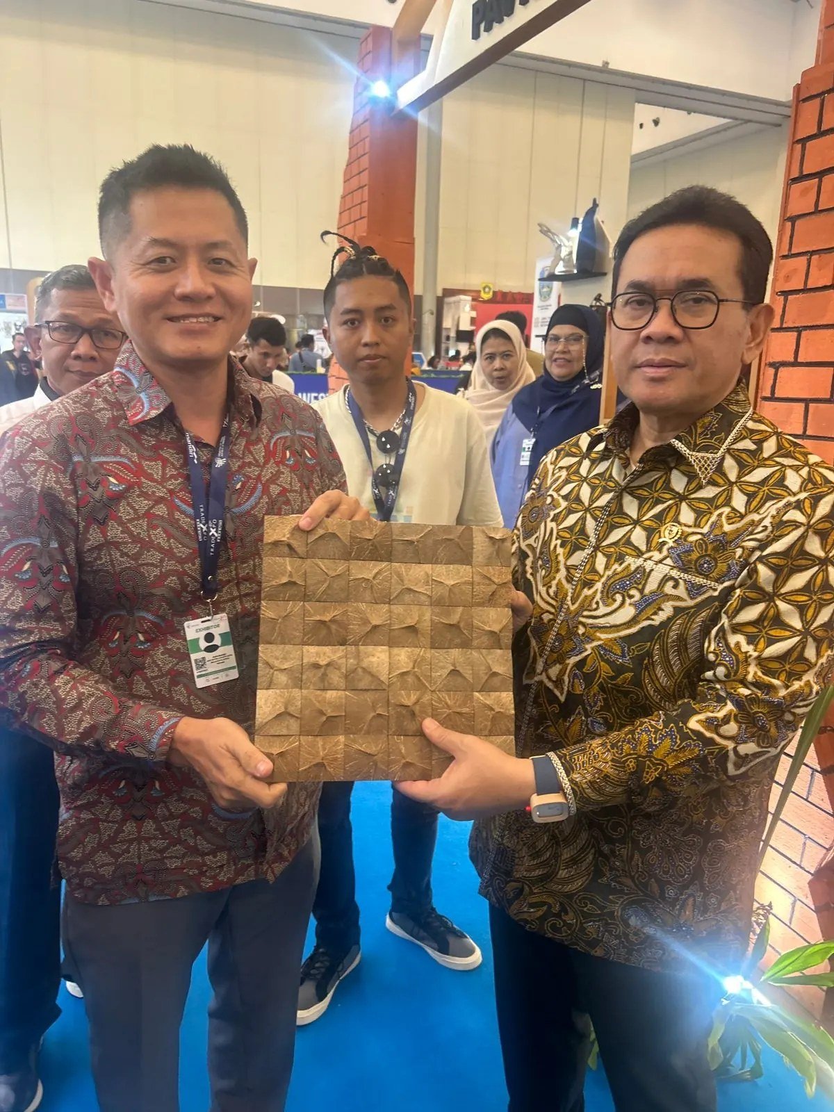 SOSI exhibitor and a visitor jointly holding a coconut shell mosaic wall panel sample at Trade Expo Indonesia 2025 Indonesia Pavilion
