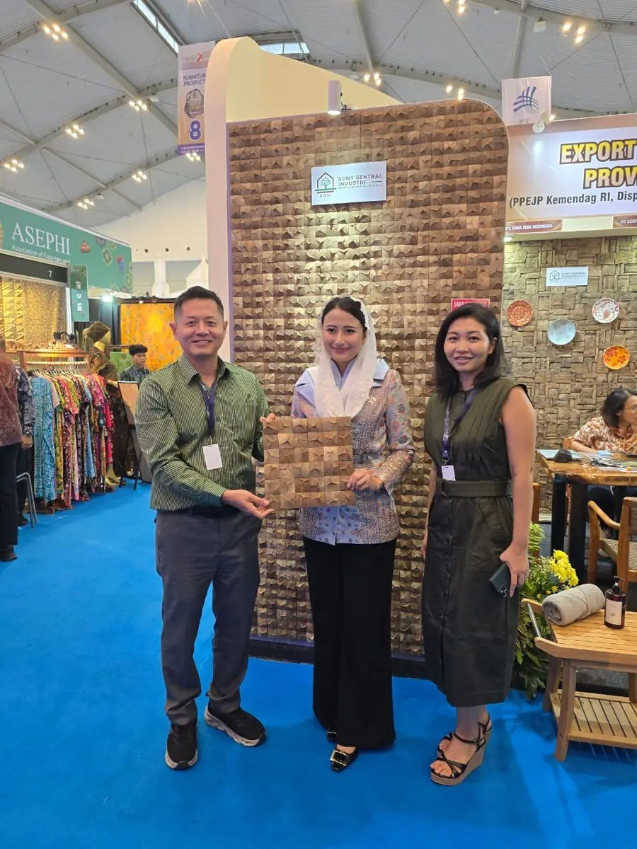 Three people holding a square 3D teak wall panel sample in front of the SOSI mosaic display wall at Trade Expo Indonesia 2025
