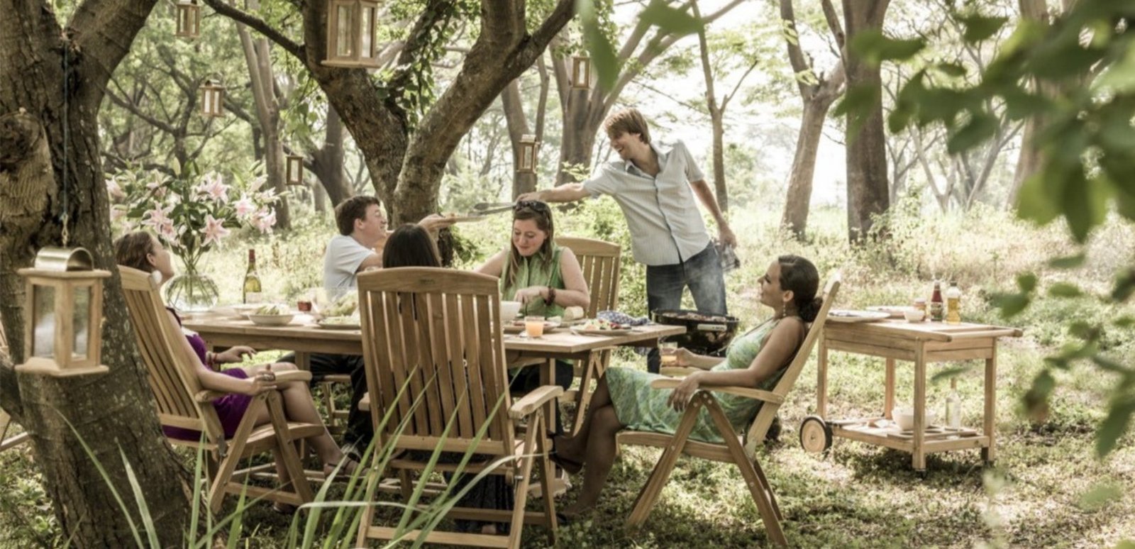 Family at a teak garden dining table with folding chairs under the trees